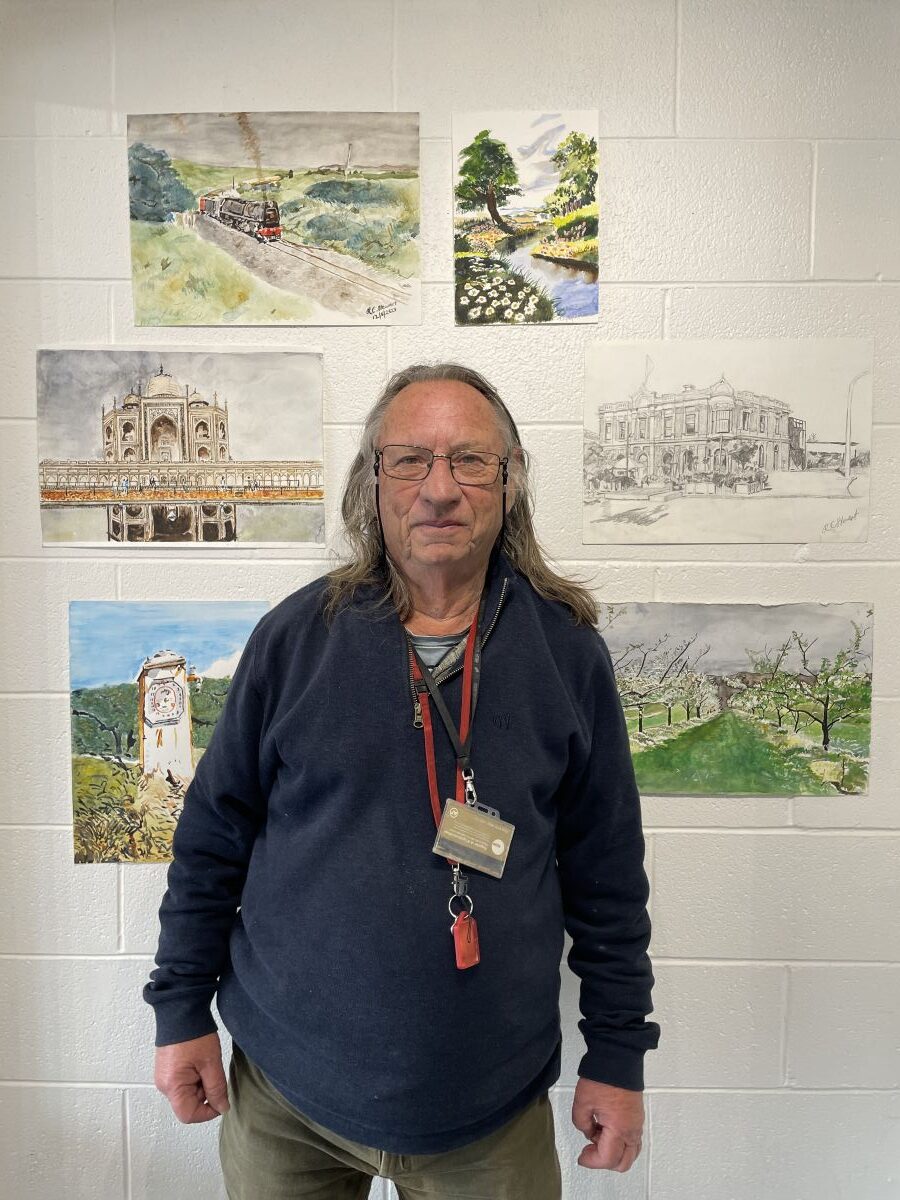 Raymond Stewart standing in front of his paintings