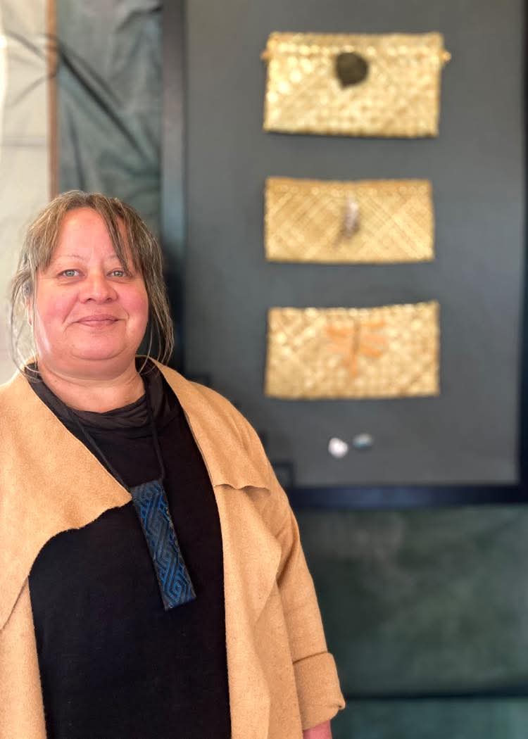 Lisa Critchley Lisa Critchley, Toi Hono Tutor at Toi Ora, standing in front of an artwork consisting of three woven baskets on a black surface.