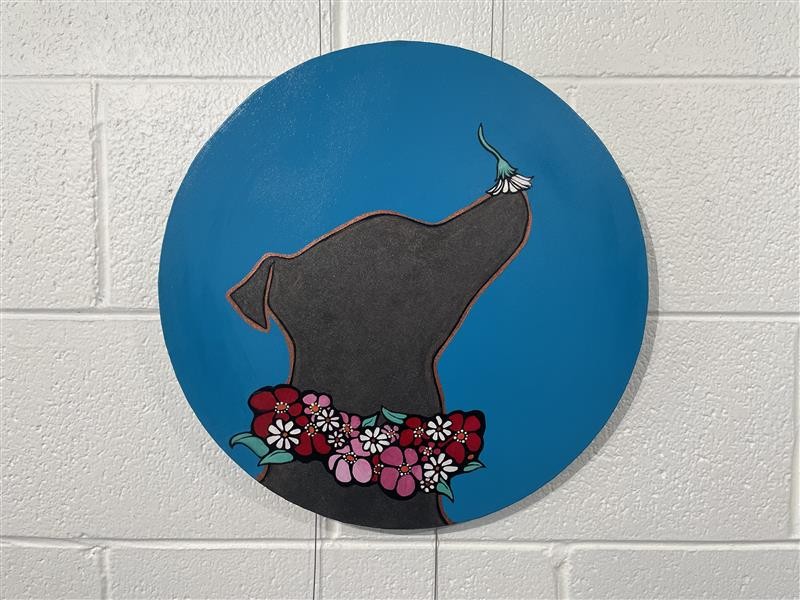 A circular painting with a black dog, red bandana and a flower on his nose.